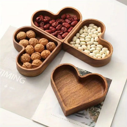Four heart-shaped wooden bowls, three filled with nuts and dried fruit, one empty, on a magazine.
