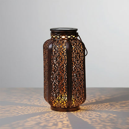 Decorative solar lantern with a dark metal filigree design casting patterned light on the surface below.