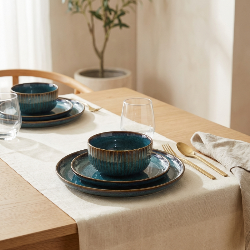 Dining table set with blue ceramic dishes, gold cutlery, and a plant in the background.