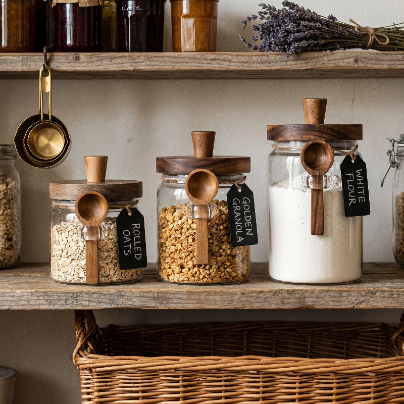 Airtight glass jars with acacia lids and spoons styled on kitchen shelves