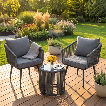 Two chairs with gray cushions and a small table on a wooden deck with a garden in the background.