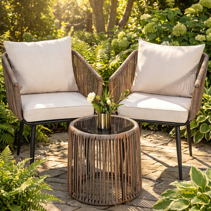 Two wicker chairs with beige cushions and a matching table on a patio surrounded by greenery.