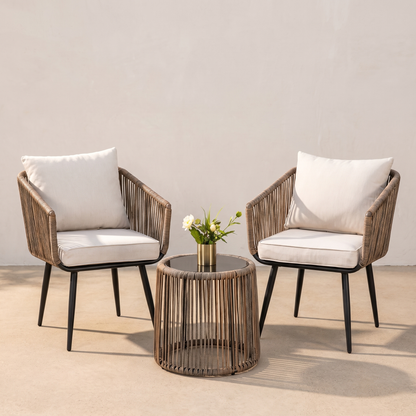 Two wicker chairs with white cushions and a matching side table on a neutral background