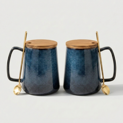Two blue ceramic mugs with wooden lids and gold spoons on a light gray background
