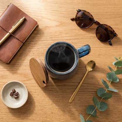Azure blue pottery mug on wooden desk beside notebook and pen