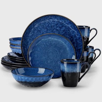 Black and blue starry-glazed ceramic dinnerware place setting with a dinner plate, salad plate, bowl, and mug on a clean off-white background