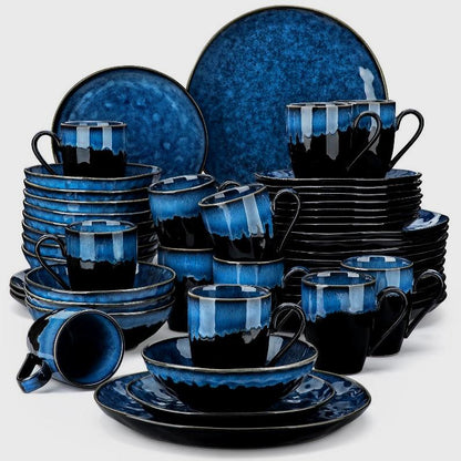 Black and blue starry-glazed ceramic dinnerware set of plates, bowls, and mugs on a clean off-white background