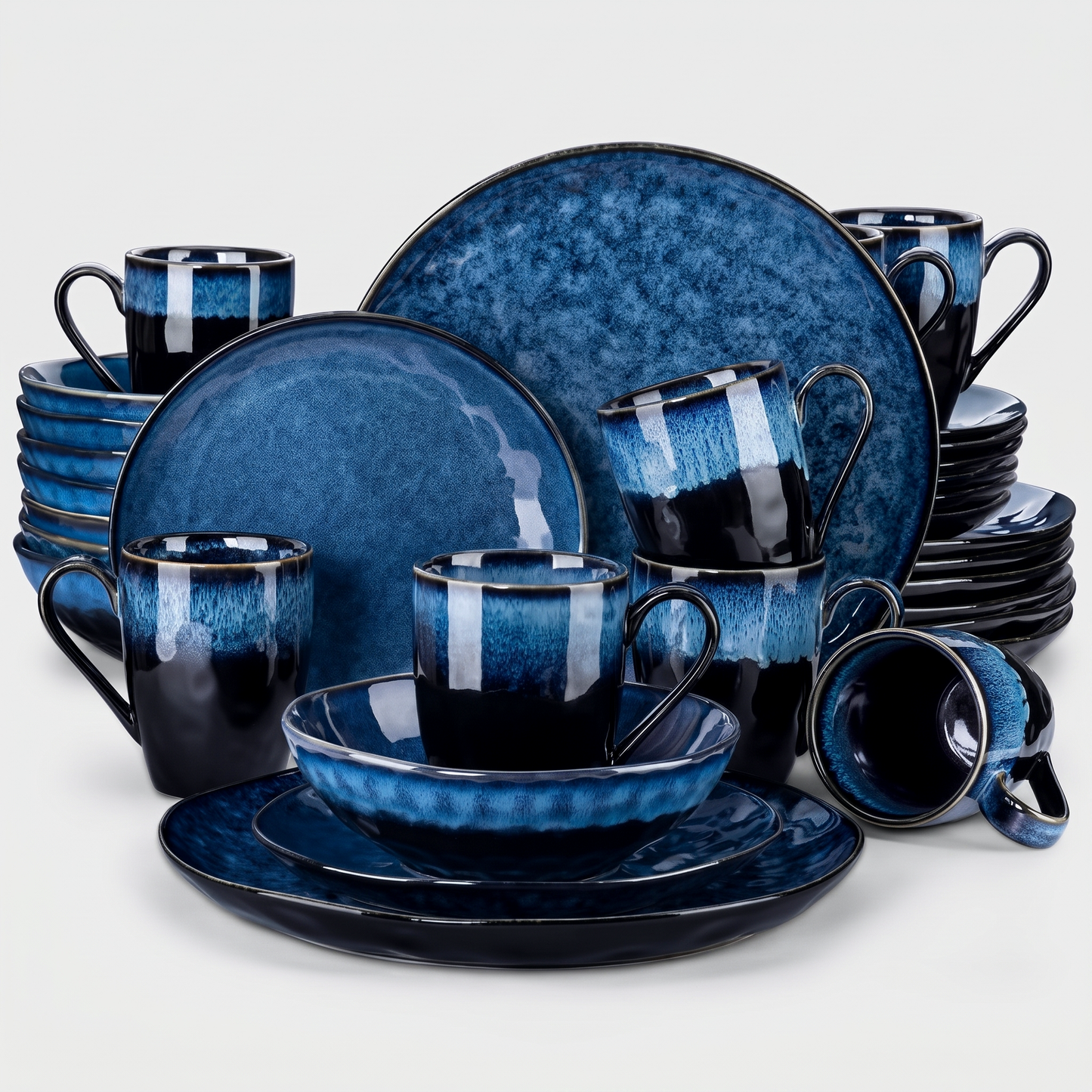 Black and blue starry-glazed ceramic dinnerware collection stacked as a set of plates, bowls, and mugs on a clean off-white background