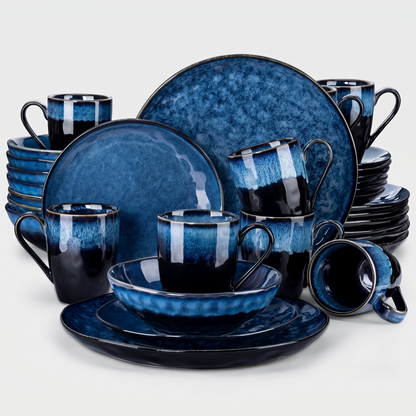 Black and blue starry-glazed ceramic dinnerware collection stacked as a set of plates, bowls, and mugs on a clean off-white background