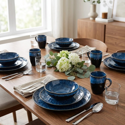Black and blue glazed ceramic dinnerware set on a wood dining table with fresh flowers