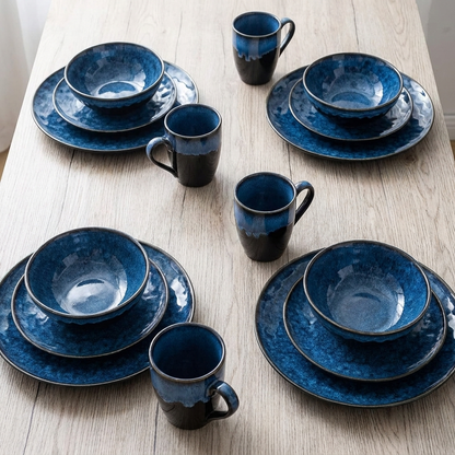 Overhead view of the black and blue glazed ceramic dinnerware set arranged on a wood table