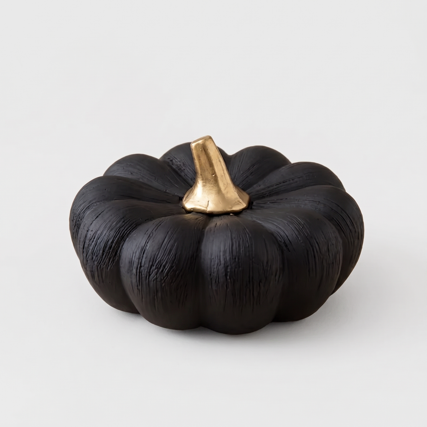 Small black decorative ceramic pumpkin with a gold stem on a clean off-white background