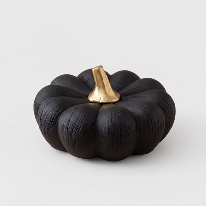 Small black decorative ceramic pumpkin with a gold stem on a clean off-white background