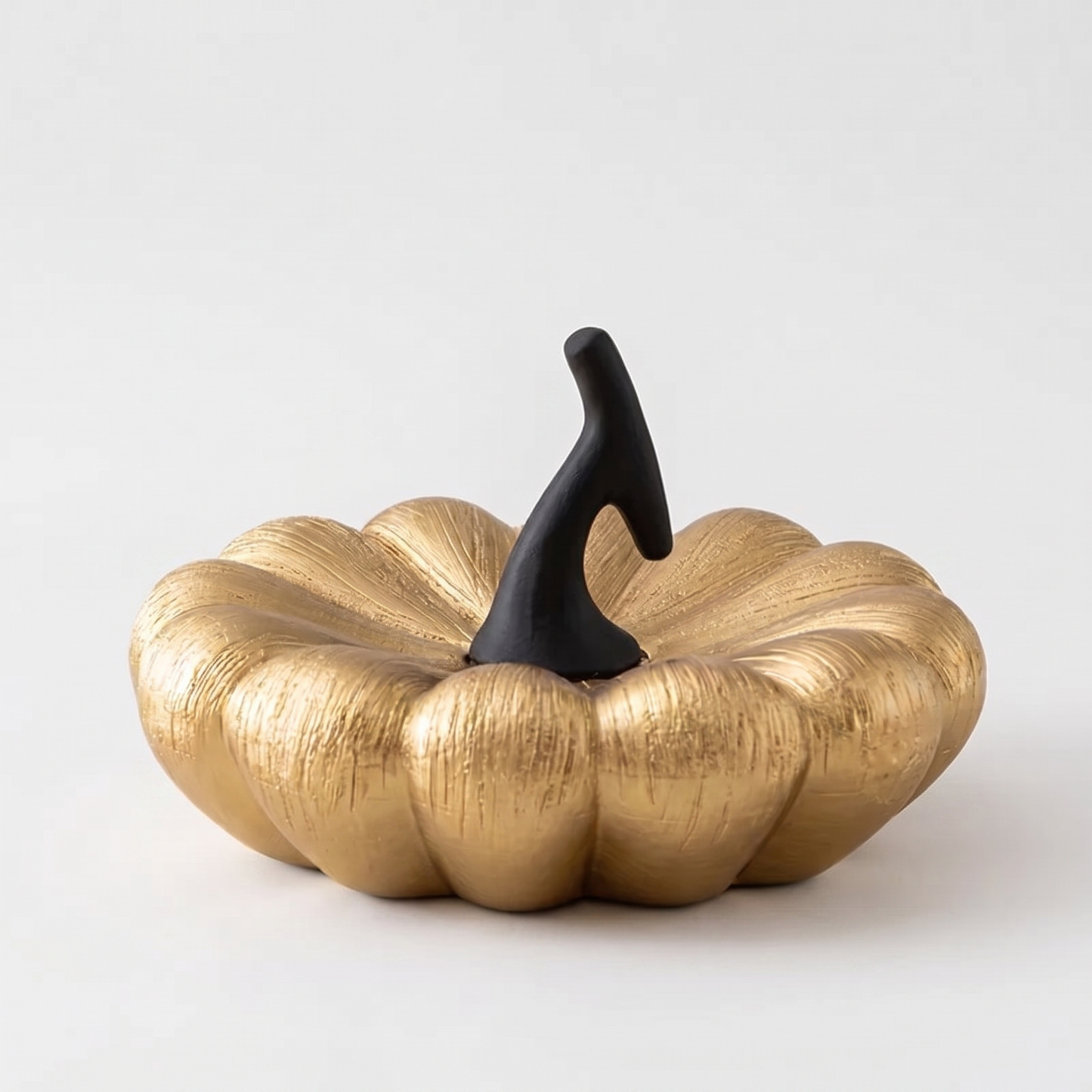 Large gold decorative ceramic pumpkin with a black stem on a clean off-white background