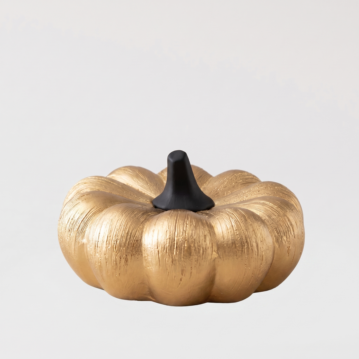Small gold decorative ceramic pumpkin with a black stem on a clean off-white background