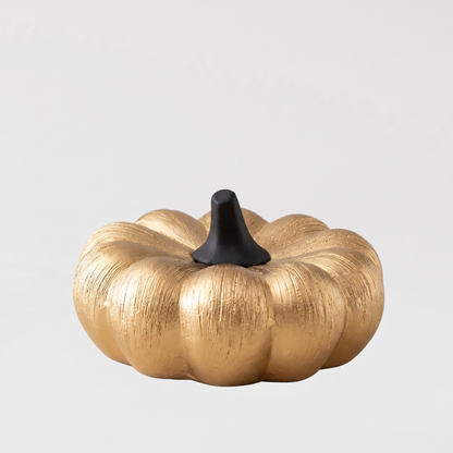 Small gold decorative ceramic pumpkin with a black stem on a clean off-white background