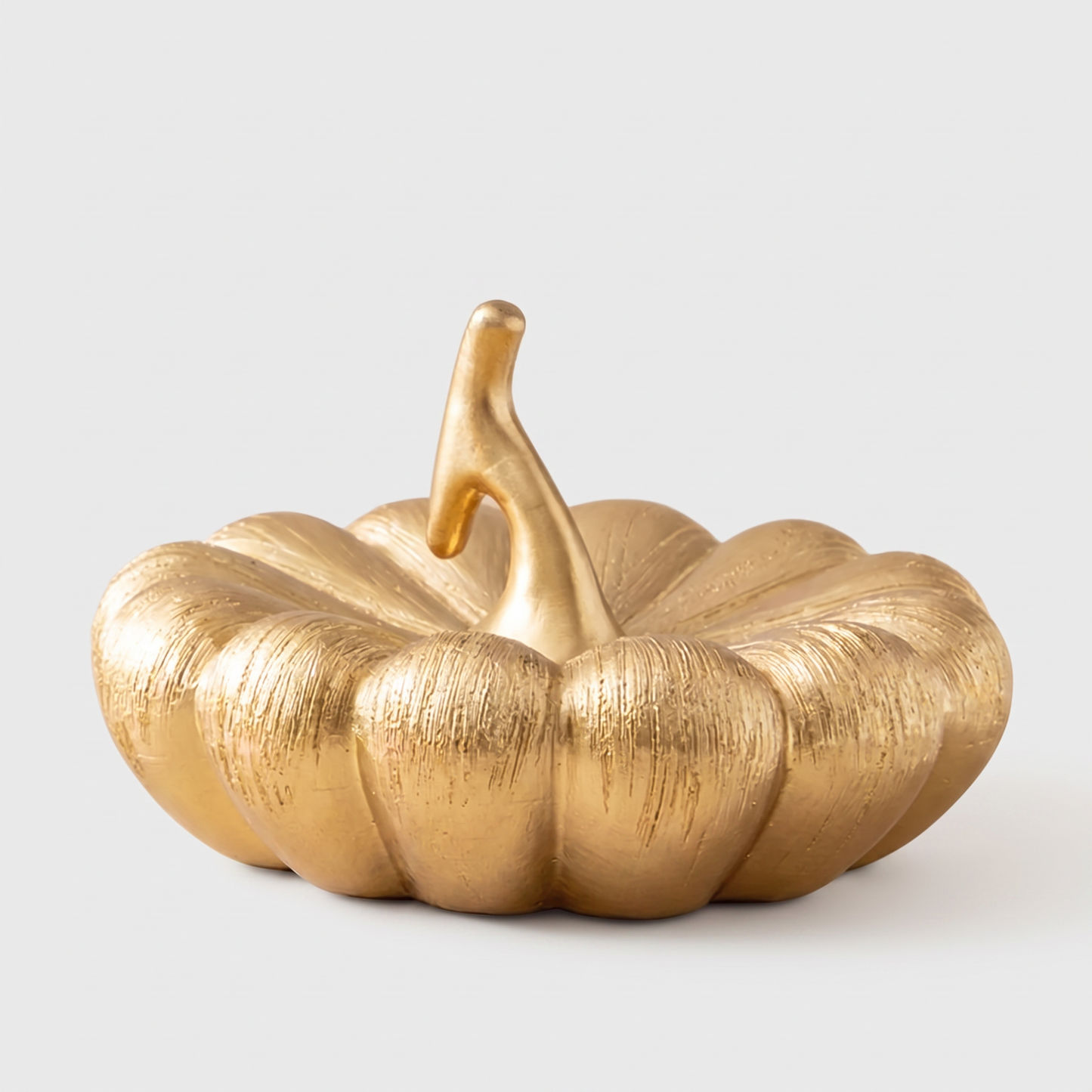Large gold decorative ceramic pumpkin with a gold stem on a clean off-white background
