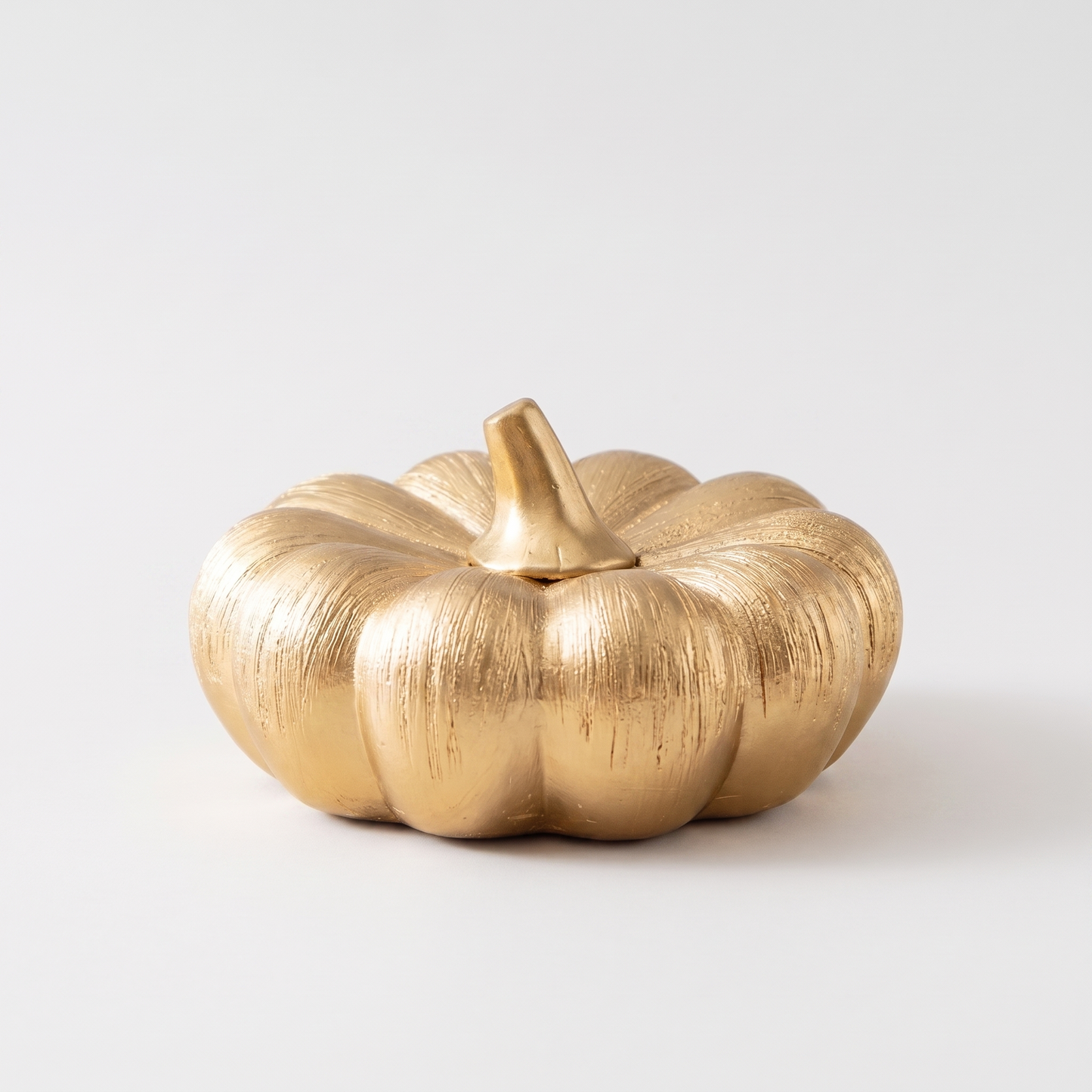 Small gold decorative ceramic pumpkin with a gold stem on a clean off-white background