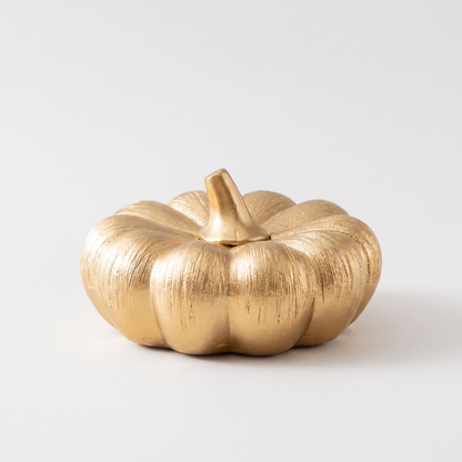 Small gold decorative ceramic pumpkin with a gold stem on a clean off-white background