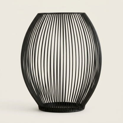 Tall black iron wire cage candleholder with a lit candle on a clean off-white background