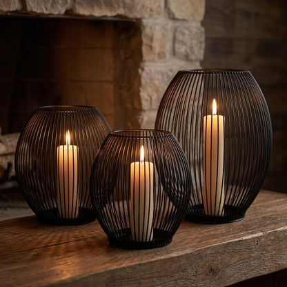 Three black iron wire candleholders with lit candles on a table by a fireplace