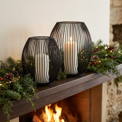 Black iron wire candleholders with lit candles on a fireplace mantel with greenery