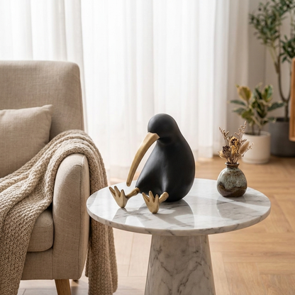 Black Kiwi Bird Sculpture displayed on a round marble side table next to an armchair