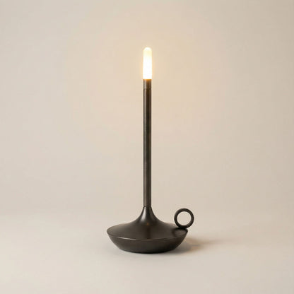 Black candle holder with a lit candle on a plain background