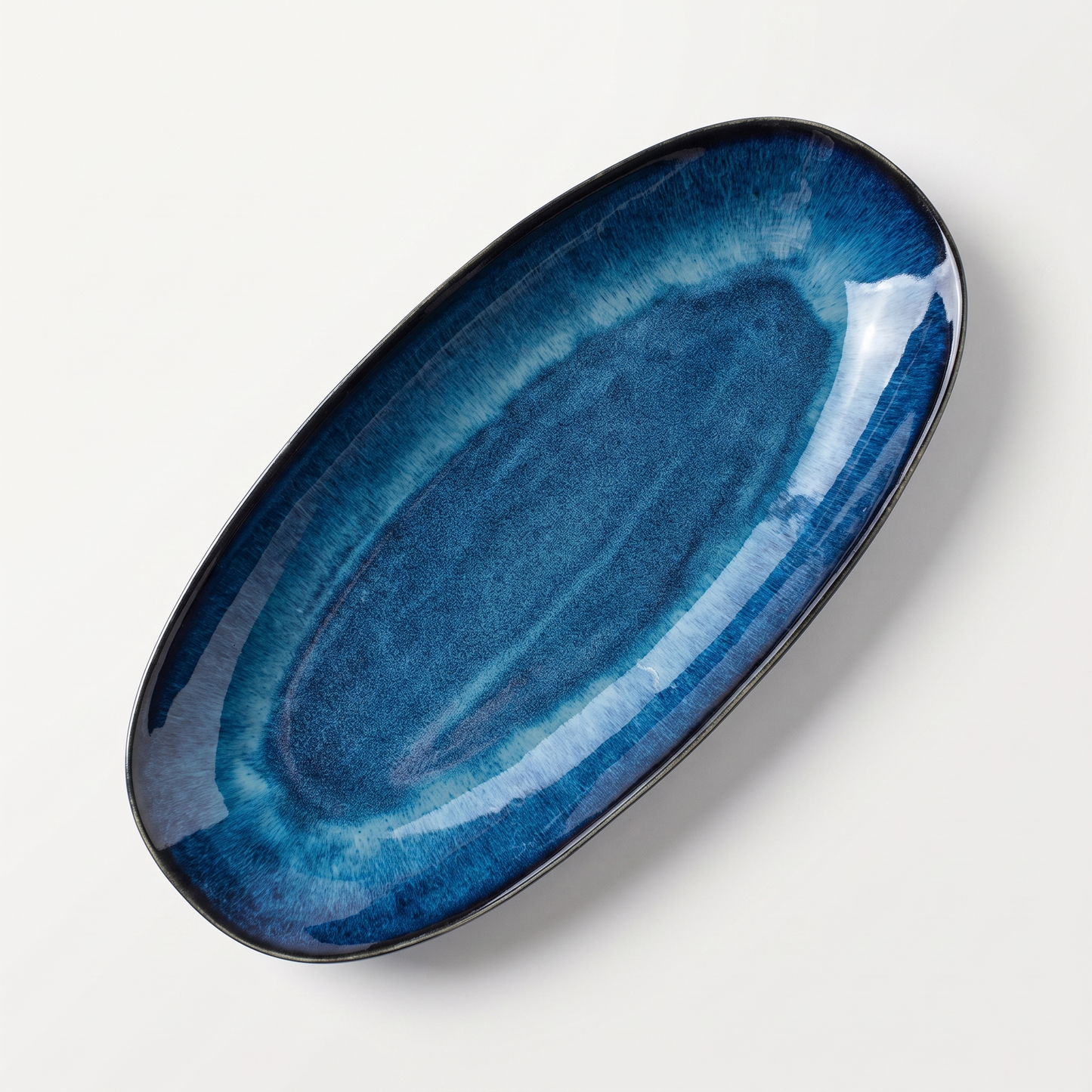 Blue kiln-glazed oval ceramic serving dish with a unique reactive glaze on a clean off-white background