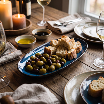 Blue kiln-glazed ceramic serving dish styled on a rustic dining table with olives and bread