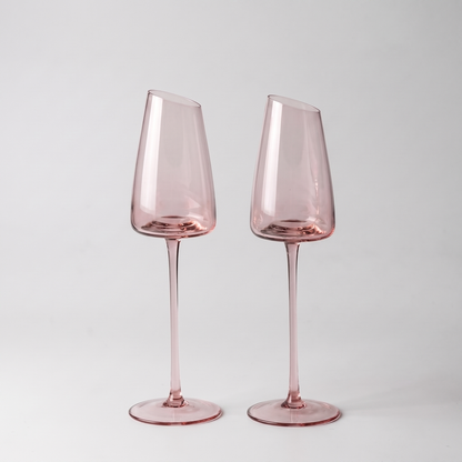 Set of 2 blush pink hand-blown crystal champagne glasses with an angled rim and pink stem on a clean off-white background