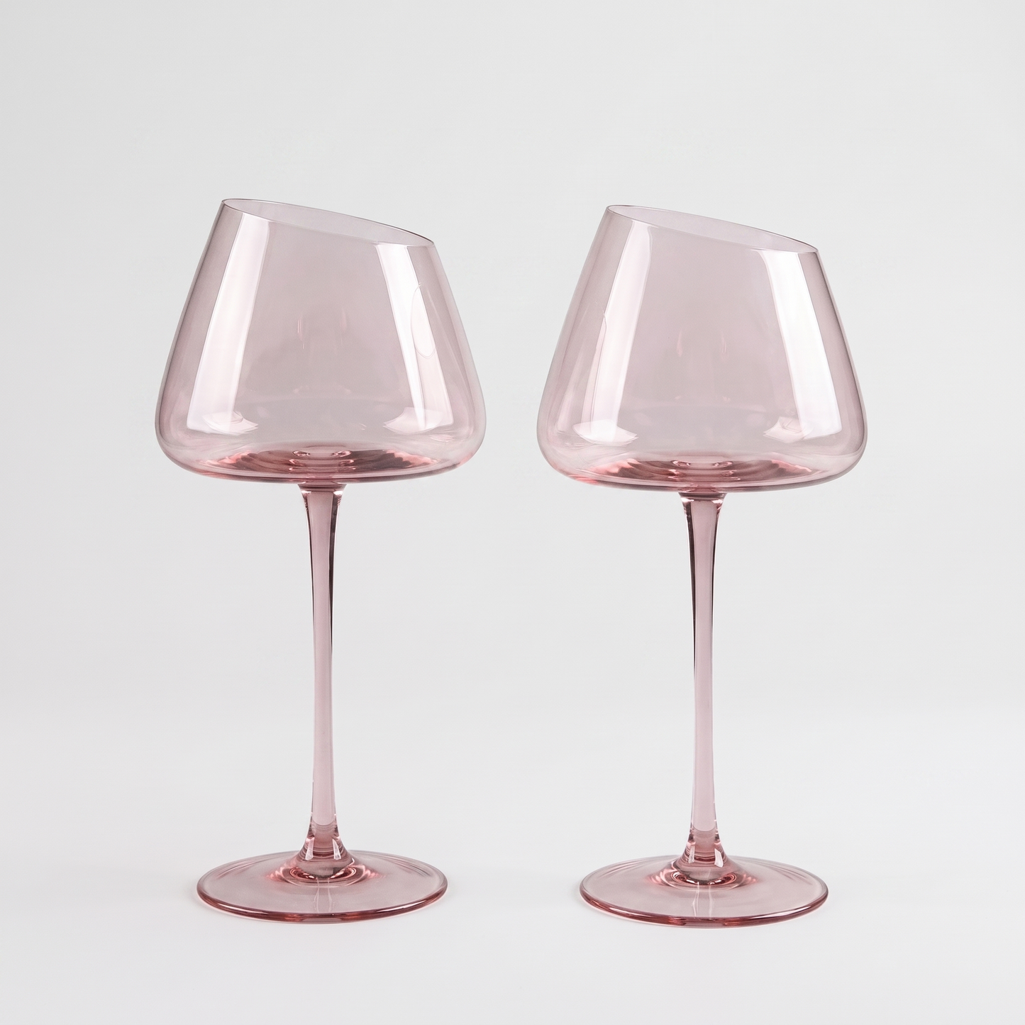 Set of 2 blush pink hand-blown crystal red wine glasses with an angled rim and pink stem on a clean off-white background