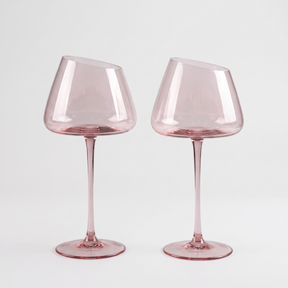 Set of 2 blush pink hand-blown crystal red wine glasses with an angled rim and pink stem on a clean off-white background