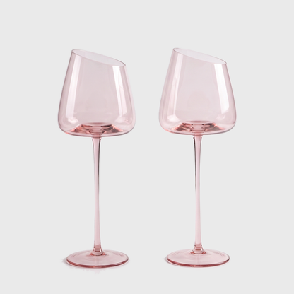 Set of 2 blush pink hand-blown crystal white wine glasses with an angled rim and pink stem on a clean off-white background