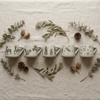 Flat lay of botanical ceramic coffee mugs arranged with eucalyptus and pinecones