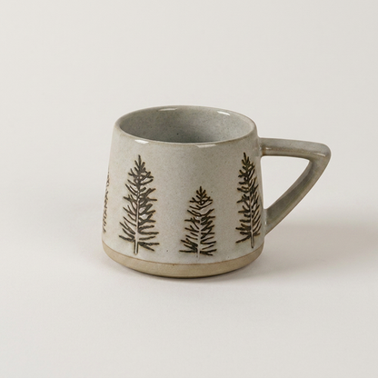 Botanical ceramic coffee mug with a hand-painted pine tree forest design on a clean off-white background