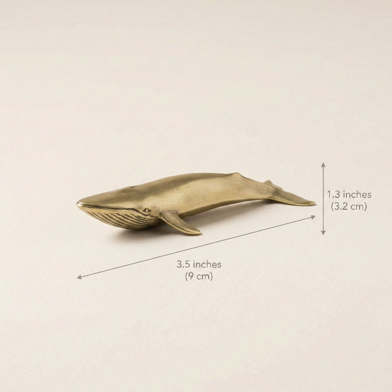 Brass whale figurine with measurements on a beige background