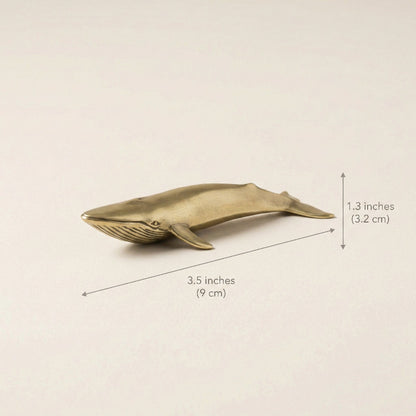 Brass whale figurine with measurements on a beige background