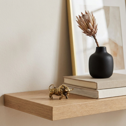 Decorative shelf with a black vase, books, and a gold bull figurine.