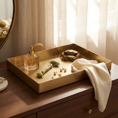 Gold tray with a bottle of perfume, jewelry, and a towel on a wooden surface.