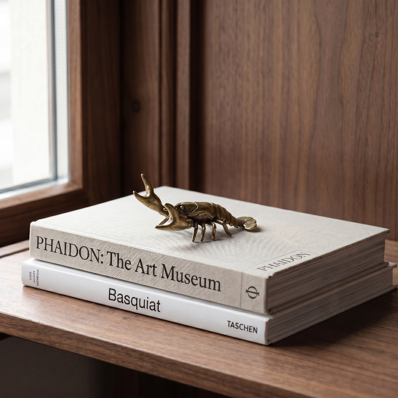 Brass crayfish figurine on stacked books by window