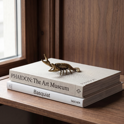 Brass crayfish figurine on stacked books by window