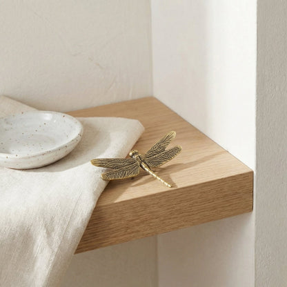 Brass dragonfly decorative item on a wooden surface with a white dish and cloth.