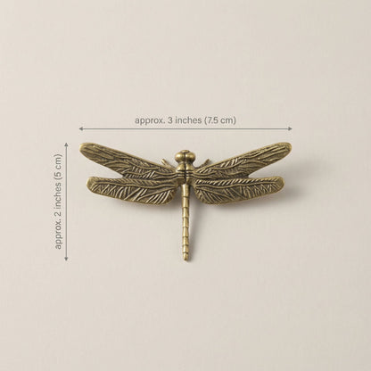 Bronze dragonfly-shaped object with measurements on a beige background