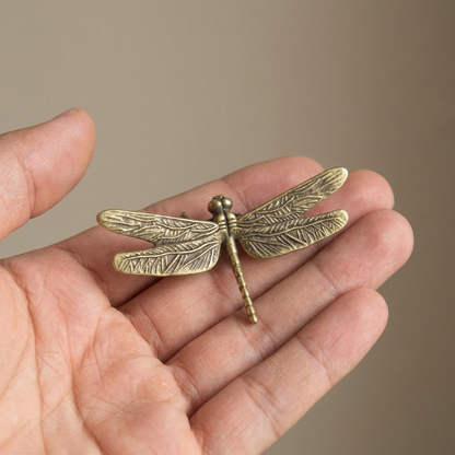 Small brass dragonfly figurine shown in hand for scale