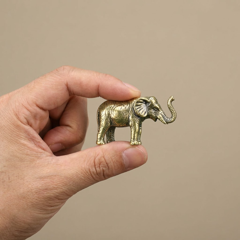 Hand holding a small gold elephant figurine against a beige background