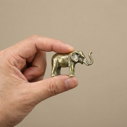 Hand holding a small gold elephant figurine against a beige background