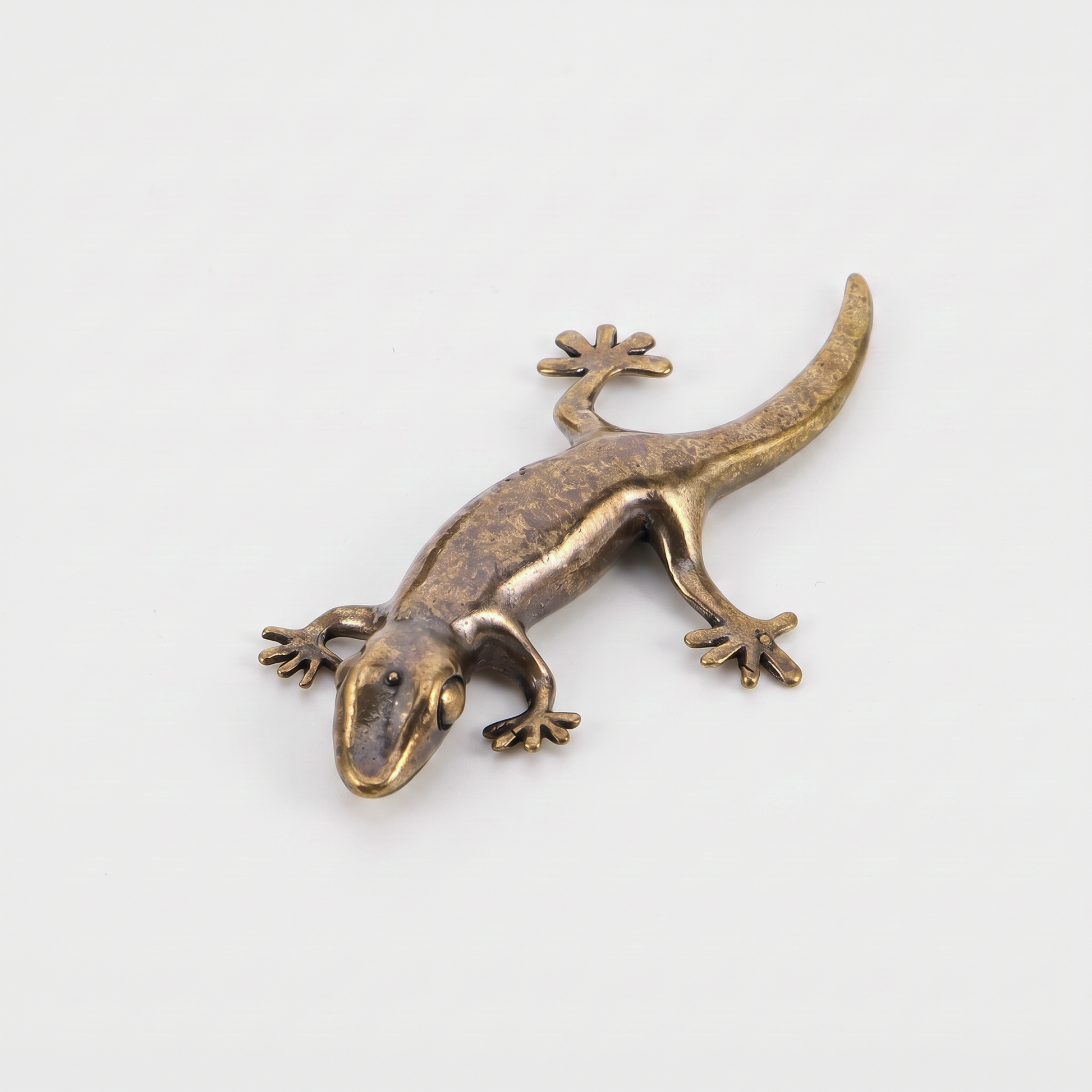 Brass gecko figurine on an off-white background