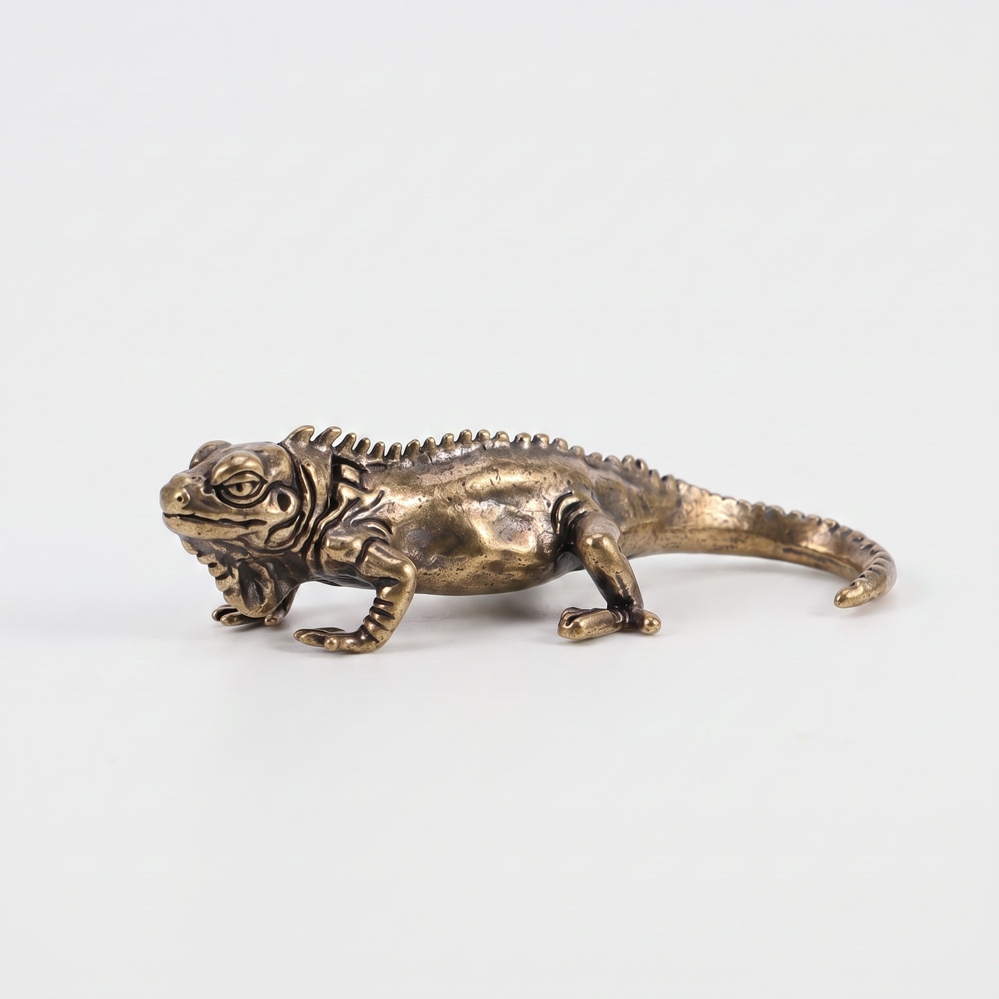 Brass iguana figurine on an off-white background