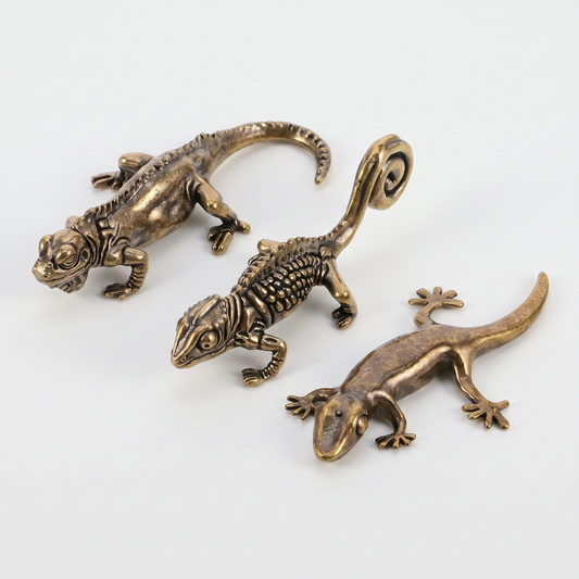 Set of three brass reptile figurines (chameleon, iguana, gecko) on an off-white background